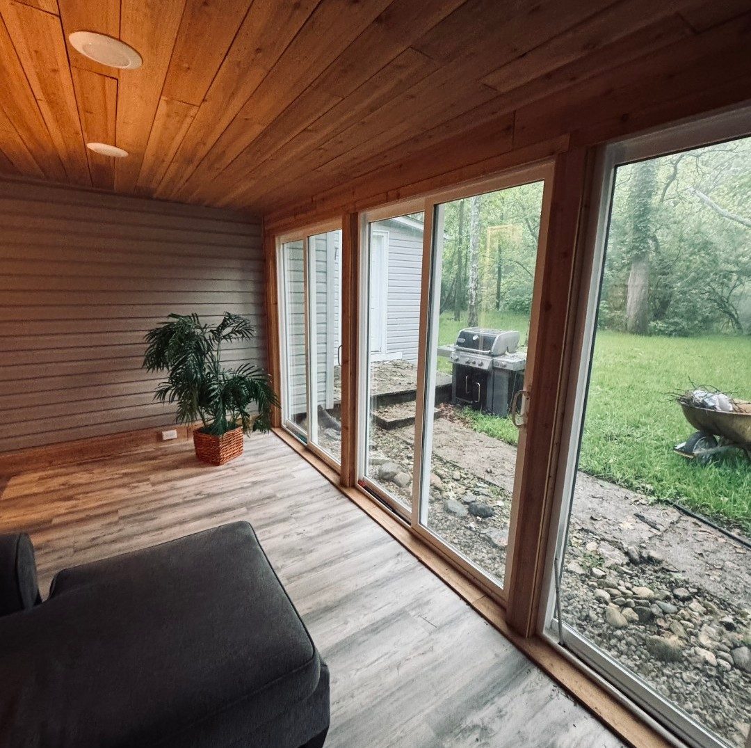 Cedar sunroom with a wall of sliding glass doors opening to the wooded backyard at the Bear Creek recovery home, Miamisburg Ohio